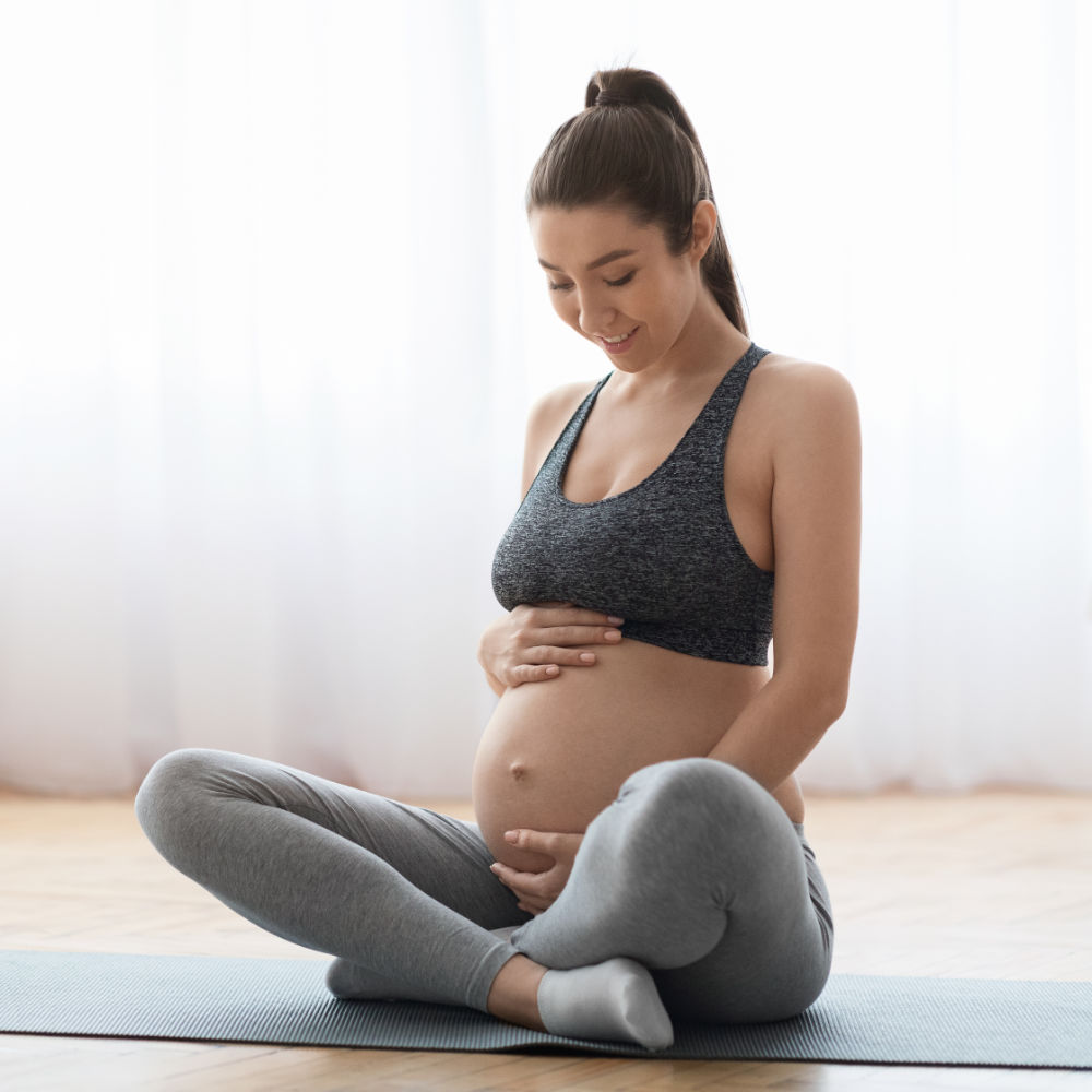 Schwangere Frau sitzt auf einer Yogamatte