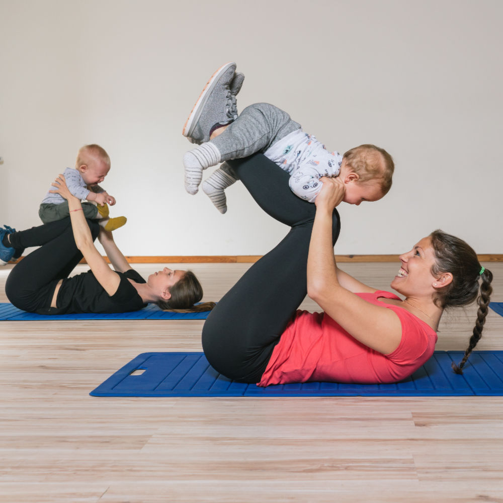 Zwei Babys krabbeln auf den Beinen ihrer Mütter bei einer Yogaübung