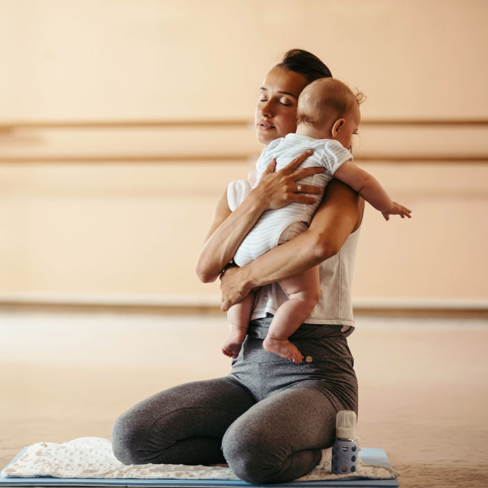 Mutter hält beim Mama-Baby -Yoga ihr Kind in den Armen